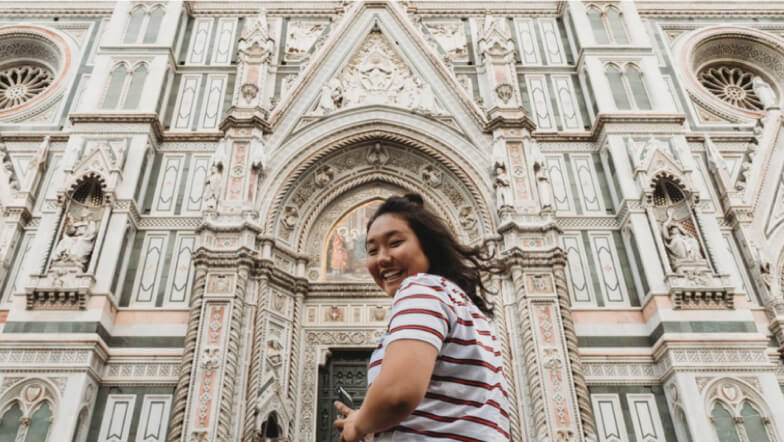 A woman looking at the camera while standing in front of a large cathedral