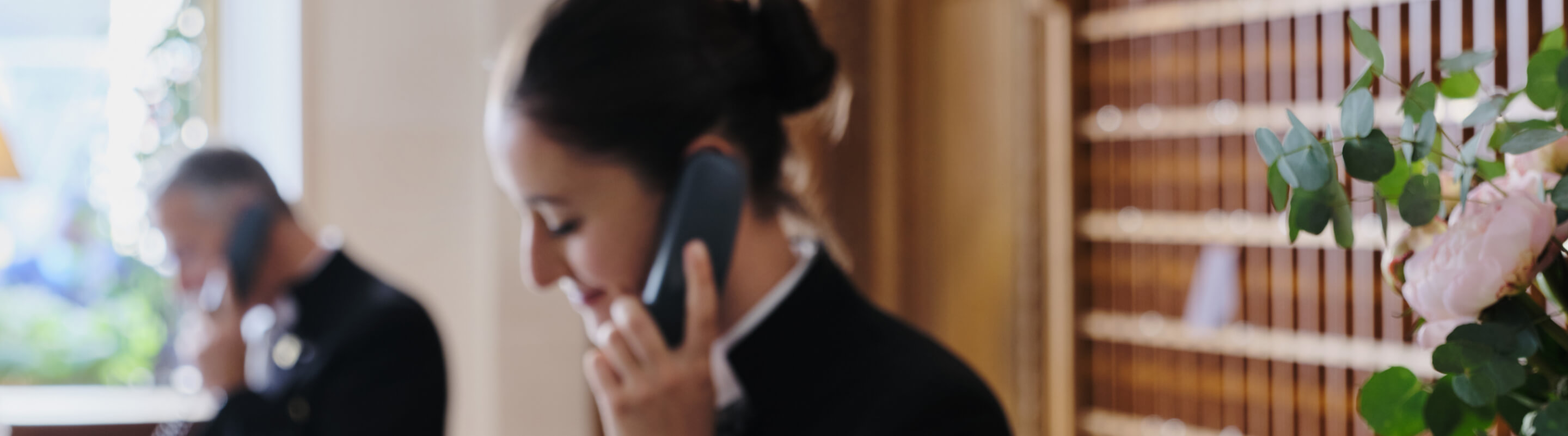 Two hotel concierges help guests over the phone at the front desk.