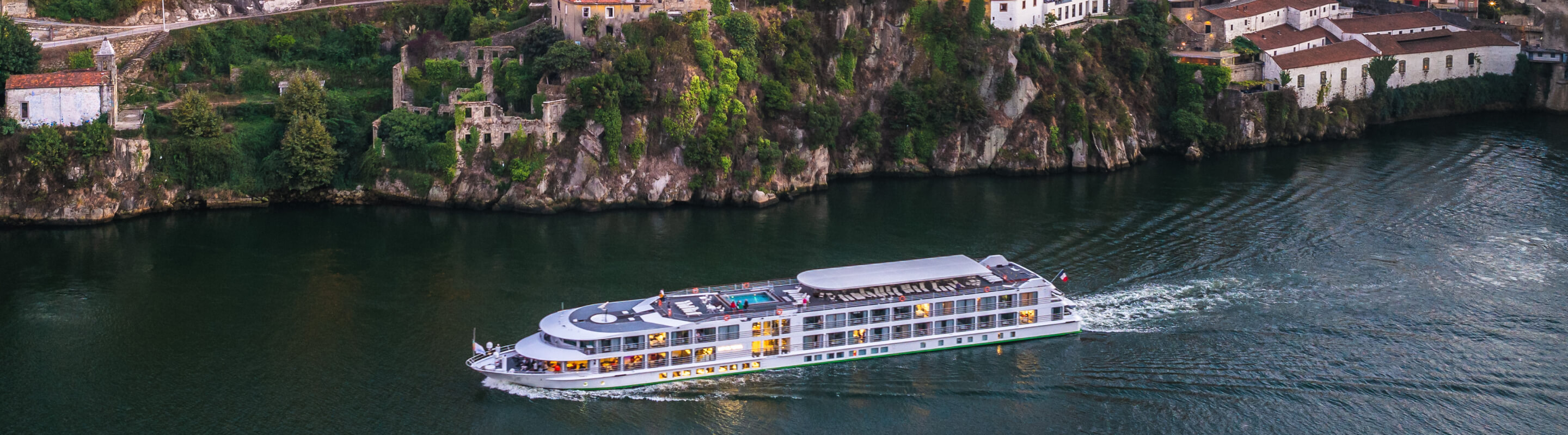 Um navio de cruzeiro fluvial navegando perto de uma margem ao anoitecer.