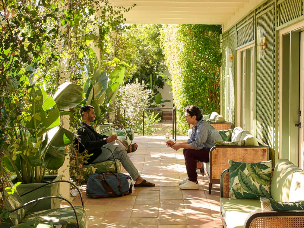 Two people sitting across from each other on benches having a conversation with luggage at their sides.