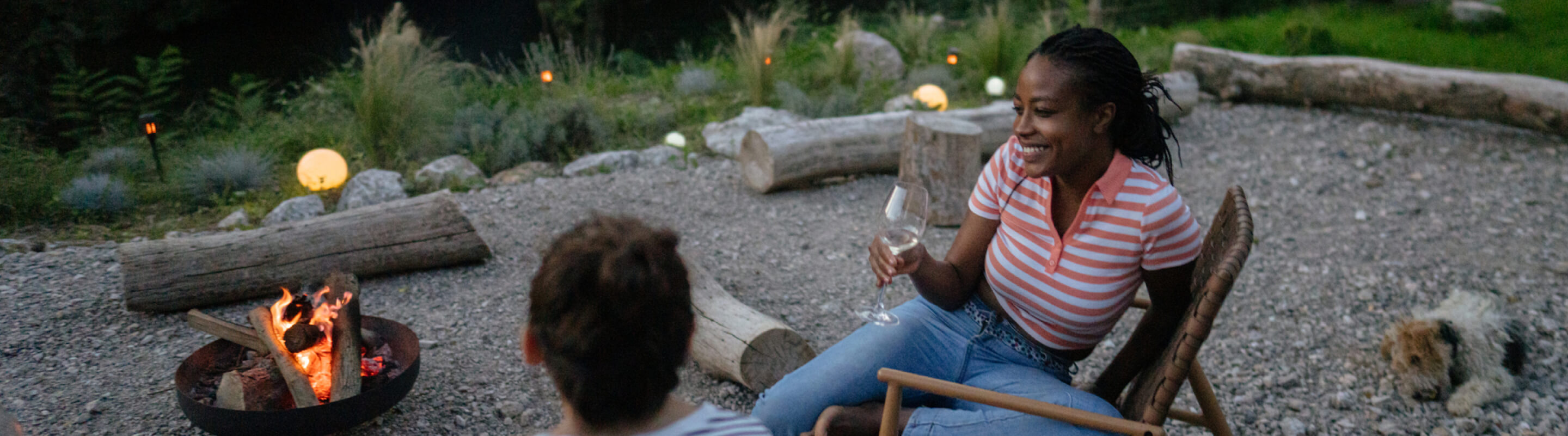 A woman drinking wine next to a burning campfire.