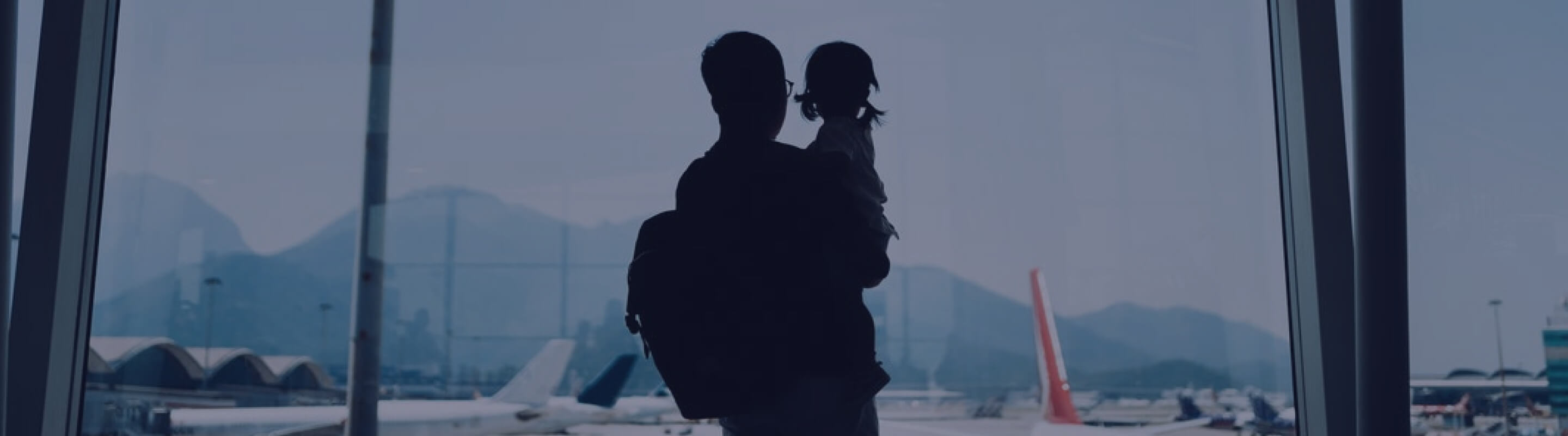 A man holds a child as they look out of an airport window. 