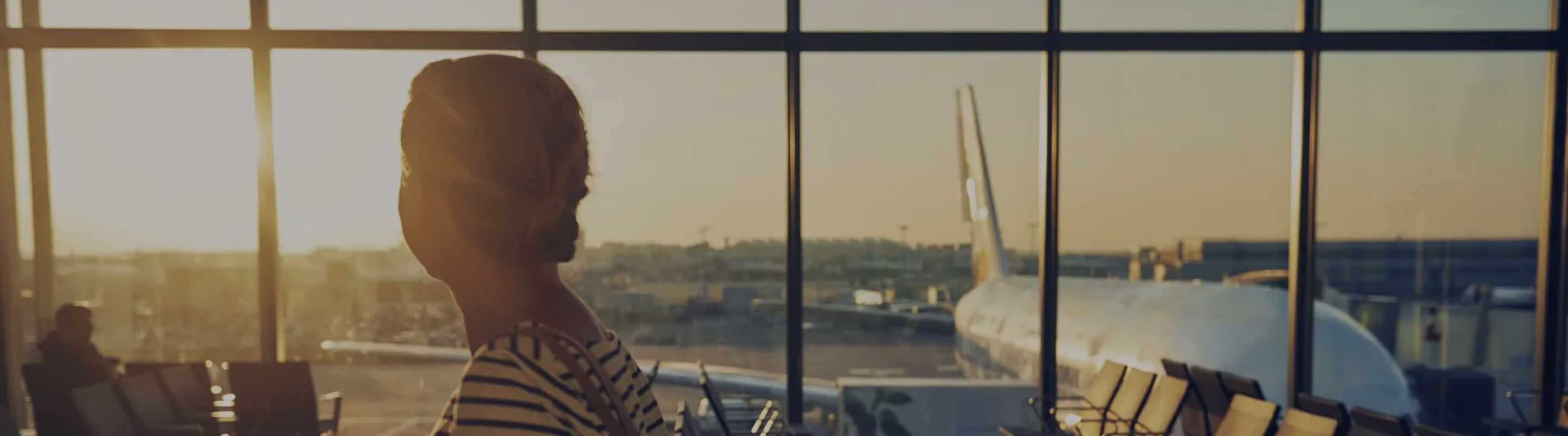 A woman looks out of an airport window at waiting planes.