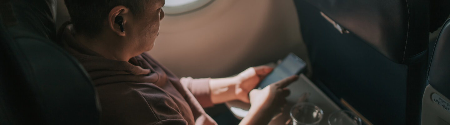 A man looks at his mobile phone while sitting in an aeroplane seat.
