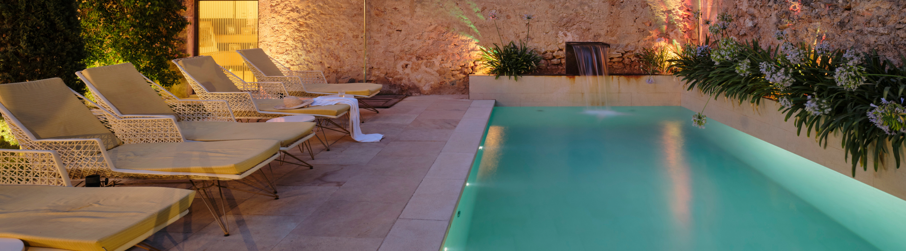 Swimming pool and patio at Sa Creu Nova hotel illuminated at night.